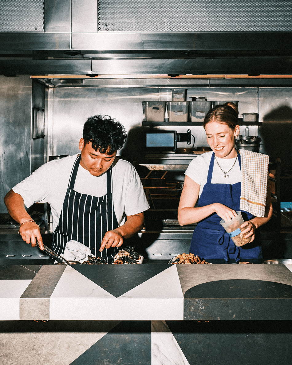 atis chef preparing healthy salad toppings at stainless‑steel counter, wearing striped and navy aprons