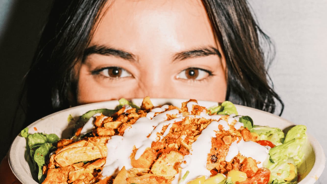 Person holding an atis bowl with blackened chicken, creamy white dressing, avocado, romaine and cherry tomatoes at an atis London restaurant