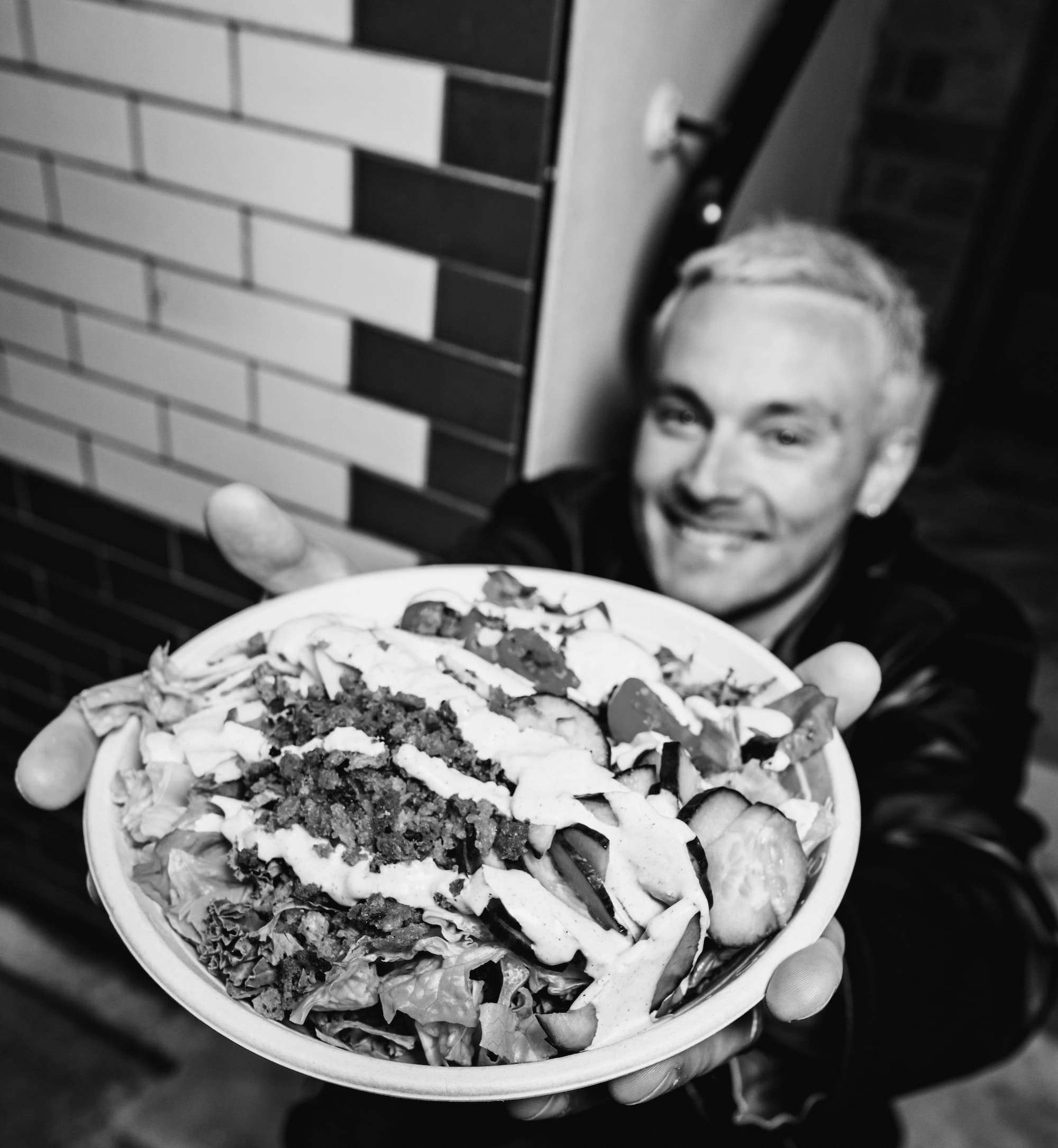 Person holding an atis bowl with roasted aubergine, mixed leaves, creamy dressing and crispy toppings inside an atis London restaurant