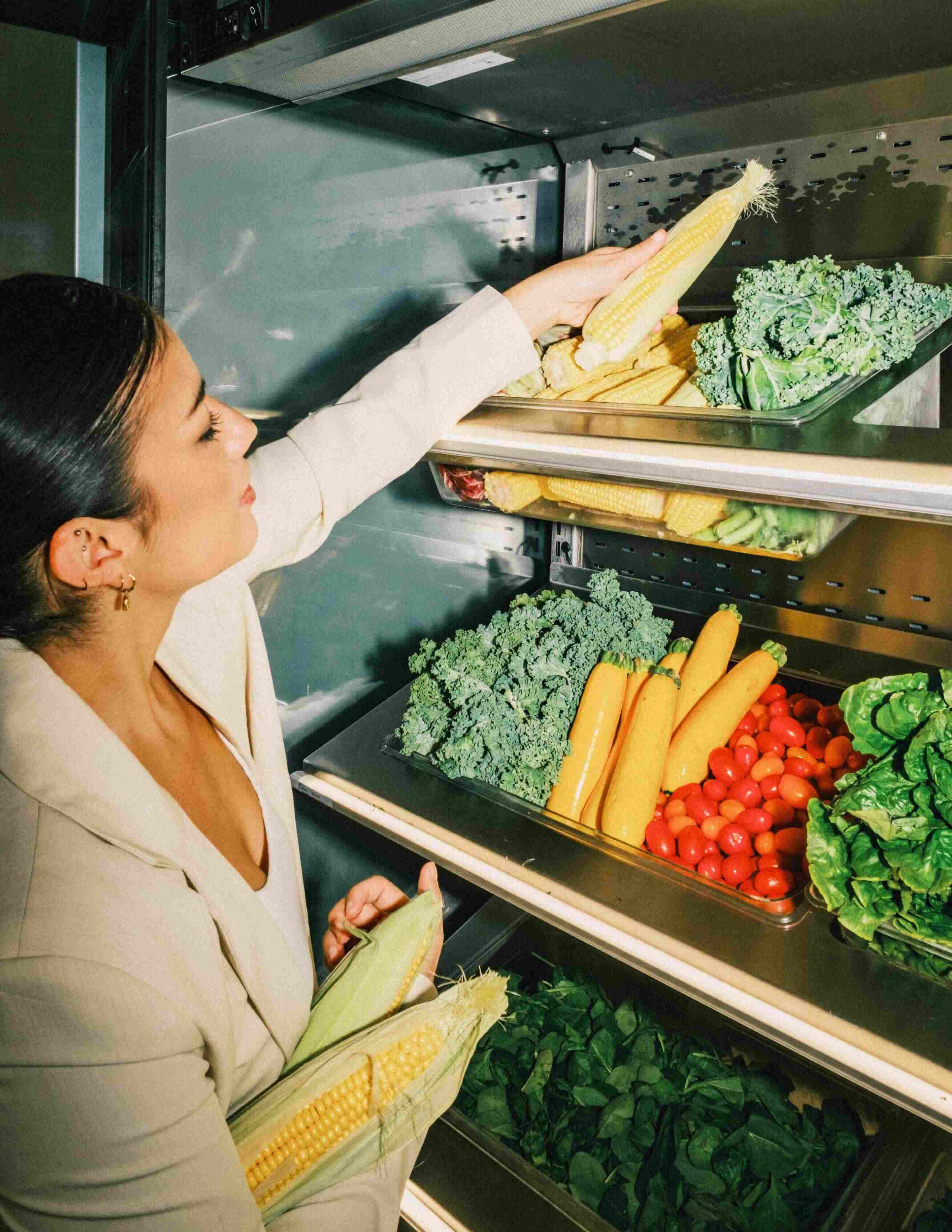 Team member selecting fresh corn from a display of seasonal vegetables including kale, tomatoes, and courgette in the atis prep kitchen