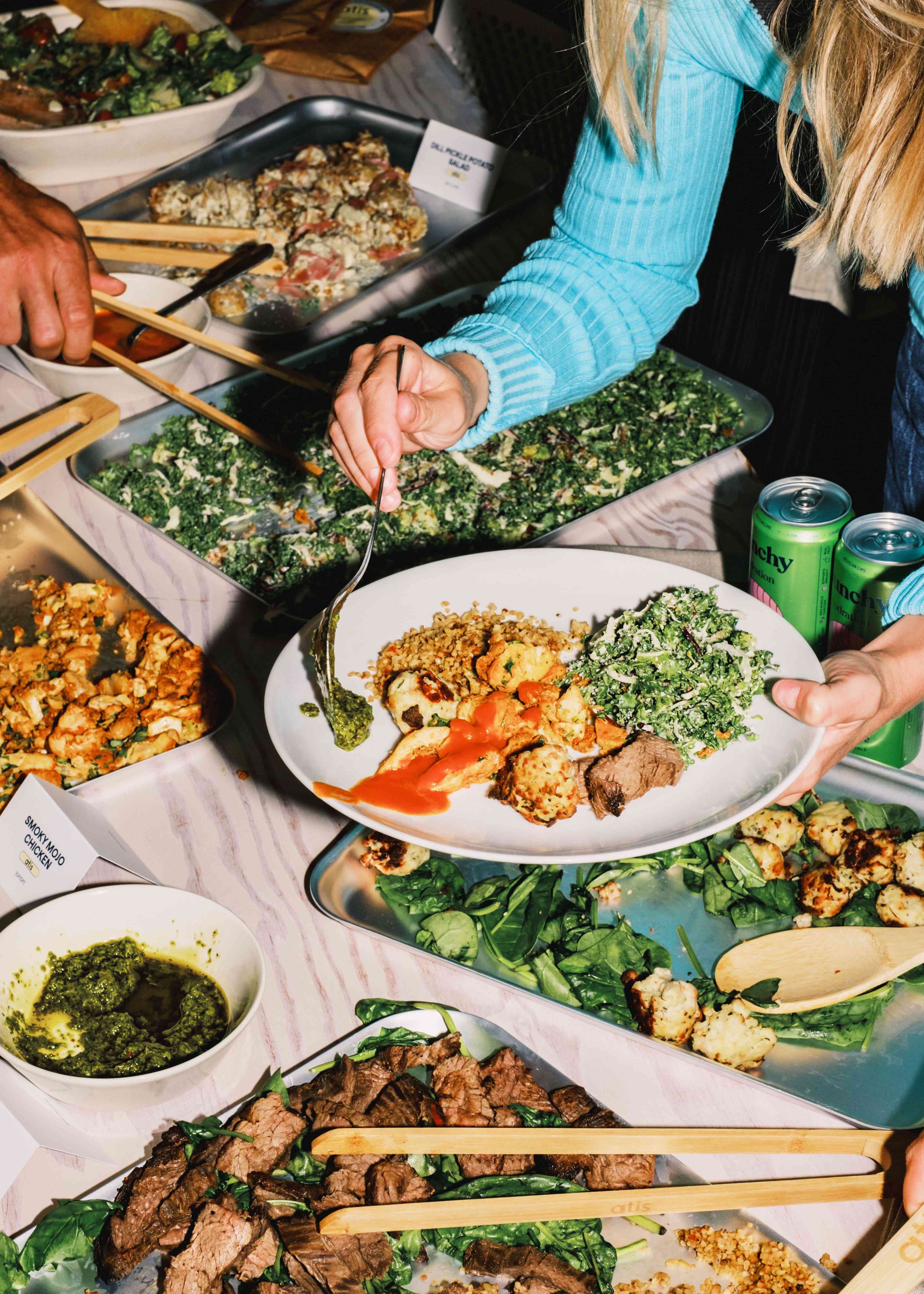 Close‑up of hand plating atis catering dish with steak, kale salad and turkey kofte on a white platter